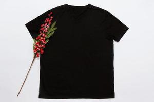 Schließen Sie herauf schwarzes leeres Schablonent-shirt mit Kopienraum und Weihnachtsfeiertagskonzept. Draufsichtmodellt-shirt und rote Feiertagsdekorationen auf weißem Hintergrund. frohes neues jahr zubehör. Weihnachts-Outfit foto