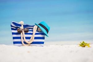 Strandzubehör - blaue Tasche, Strohhut, Sonnenbrille am weißen Strand foto