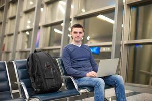 junger Mann mit Laptop und Rucksack am Flughafen foto