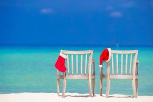roter weihnachtsstrumpf und weihnachtsmütze auf stuhl am tropischen weißen strand foto