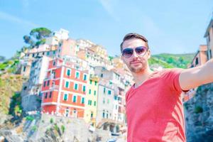 junger mann, der selfie mit schöner aussicht auf das alte italienische dorf riomaggiore, cinque terre, ligurien, italien macht. europäisch italienischer urlaub. foto