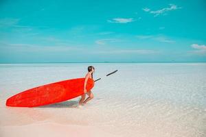 Schöne Surferin bereit zum Surfen im türkisfarbenen Meer, auf Stand-Up-Paddle-Board im exotischen Urlaub foto