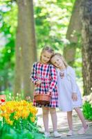 Frühlingsgarten, Frühlingsblumen, entzückende kleine Mädchen und Tulpen. süße Kinder mit einem Korb im blühenden Garten an warmen Tagen foto