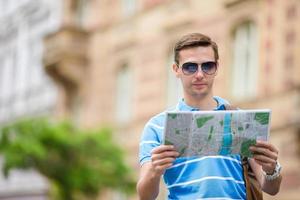 mann tourist mit stadtplan und rucksack in der europastraße. kaukasischer junge, der mit karte der europäischen stadt schaut. foto