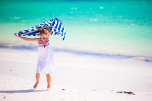 kleines mädchen hat spaß mit strandtuch während tropischer ferien foto