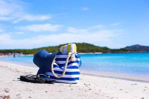 Strohhut, Tasche, Sonnenbrille und Handtuch am weißen tropischen Strand foto