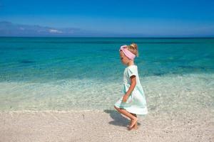 süßes kleines Mädchen, das im seichten Wasser am weißen Strand spielt foto