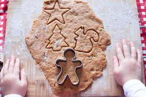 Kinderhände, die vom Teig-Lebkuchenmann für Weihnachten machen foto