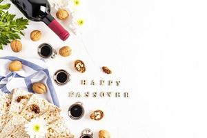 festlicher Hintergrund des jüdischen Pessachfestes mit Matza, rotem koscherem Wein und silbernen Gläsern, Nüssen auf weißem Hintergrund mit dem Text happy passah. foto