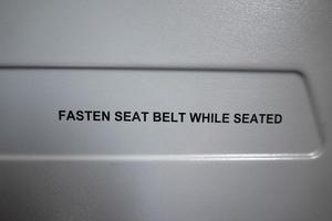 Sicherheitsgurt anschnallen, während Flugzeugschild sitzt foto