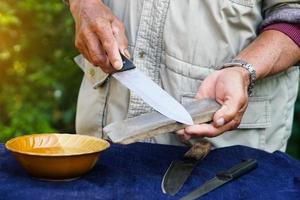 Nahaufnahme Mannhände schärfen Messer auf Wetzsteinschärfer oder Schleifstein. Konzept, Wartungswerkzeuge zum Kochen, Messer scharf machen, nicht stumpf für lange Lebensdauer. origineller Stil. foto