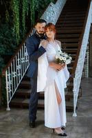 Braut in einem weißen Kleid mit Blumenstrauß und der Bräutigam in einem blauen Anzug foto