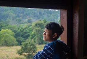 Junge, der aus dem Fenster blickt und den grünen Wald betrachtet foto