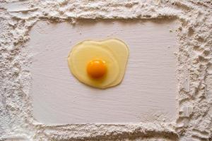 Mehl auf einen Holztisch gestreut, mit einem glatten rechteckigen Aufdruck und einem rohen Ei in der Mitte. Platz kopieren. foto