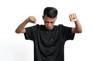 asiatischer Mann mit schwarzem Trainings-T-Shirt, der eine starke Haltung mit erhobenen Armen und Muskeln zeigt. durch weißen Hintergrund isoliert foto