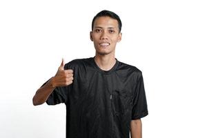 asiatischer mann, der schwarzes trainingst-shirt trägt, sich glücklich fühlt und daumen hoch gibt. durch weißen Hintergrund isoliert foto