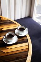 Zwei moderne Tassen Espresso auf einem Holztisch, ein Tisch vor dem Fenster. Kaffeepause. foto