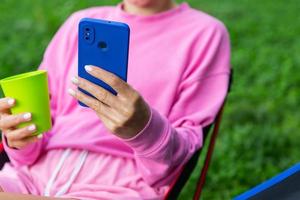 junge freiberuflerin ganz in rosa sitzt auf einem stuhl im freien, entspannt sich und nutzt das smartphone für die arbeit. das Konzept der Fernarbeit. foto