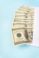 Geldversteck in Dollarscheinen, die aus einem Umschlag auf blauem Hintergrund kommen. das konzept von gehalt, bestechung, darlehen, schulden, gewinn. foto
