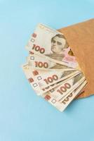 Ein Haufen Geld in 100-Griwna-Banknoten, die aus einem Umschlag auf blauem Hintergrund kommen. das konzept von gehalt, bestechung, kredit, schulden, gewinn. foto