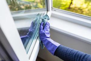 Reinigungs- und Reinigungskonzept. ein junges mädchen in lila handschuhen wischt den staub auf der fensterbank und dem fenster mit einem lappen ab. foto