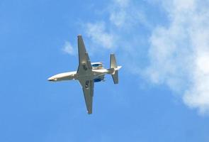 Ein zweistrahliger Business-Jet mit ausgefahrenem Fahrwerk und eingeschalteten Landescheinwerfern vor einem Himmel mit leichten Wolken. foto