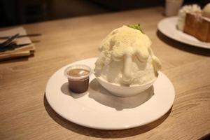 Bingsu-Dessertbonbons mit weißer Soßencreme und Kakao auf Holztablett foto