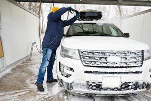 Mann wäscht Hochdruckwasser amerikanisches SUV-Auto mit Dachgepäckträger bei Selbstbedienungswäsche bei kaltem Wetter. foto