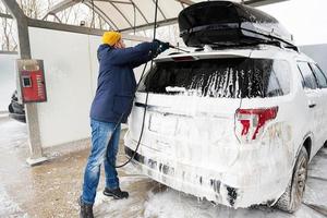 Mann wäscht amerikanisches SUV-Auto mit Dachträger in einer Selbstbedienungswäsche bei kaltem Wetter. foto