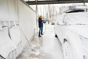 Mann wäscht amerikanisches SUV-Auto mit Dachträger in einer Selbstbedienungswäsche bei kaltem Wetter. foto