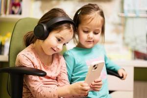 Zwei kleine Schwestern tragen Kopfhörer und schauen sich Cartoons oder Kindervideos auf dem Handy an. foto