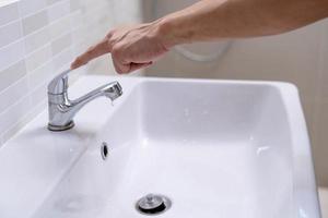 der Wasserhahn im Badezimmer mit fließendem Wasser. Mann dreht immer wieder das Wasser ab, um Wasserenergie zu sparen und die Umwelt zu schonen. wasser sparen konzept foto