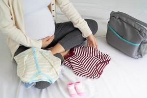 Schwangere bereiten gerne Babykleidung vor. Koffer packen, um ins Krankenhaus zu gehen foto