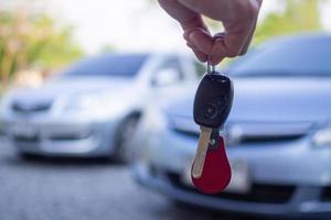 Nahaufnahme der Hand des Autobesitzers, die den Lieferschlüssel für die Käufer hält. konzept, autos zu verkaufen und neuen besitzern schlüssel zu geben. foto