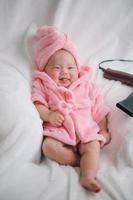 Nahaufnahme süßes neugeborenes Baby in rosafarbenem Bodysuit, das sich allein auf dem Bett hinlegt. entzückendes kind ruht auf weißen bettlaken und starrt friedlich in die kamera. Säuglings-, Gesundheitswesen und Pädiatrie, Säuglingskonzept foto