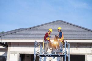 ein team asiatischer techniker installiert sonnenkollektoren auf dem dach eines hauses. Querschnittsansicht des Baumeisters im Helm, der ein Solarpanel-Systemkonzept für erneuerbare Energien installiert foto