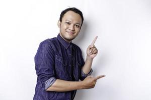 Aufgeregter asiatischer Mann mit blauem Hemd, der auf den Kopierbereich neben ihm zeigt, isoliert durch weißen Hintergrund foto