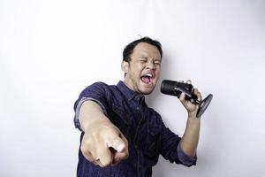 porträt eines sorglosen asiatischen mannes, der spaß beim karaoke hat und im mikrofon singt, während er über weißem hintergrund steht foto
