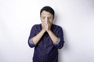 Ein Porträt eines asiatischen Mannes, der ein blaues Hemd trägt, das durch weißen Hintergrund isoliert ist, sieht deprimiert aus foto