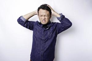 Ein Porträt eines asiatischen Mannes, der ein blaues Hemd trägt, das durch weißen Hintergrund isoliert ist, sieht deprimiert aus foto
