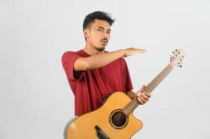 Porträt des jungen asiatischen Mannes im roten T-Shirt mit einer akustischen Gitarre, die auf weißem Hintergrund isoliert ist foto