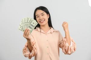 Porträt einer fröhlichen jungen Frau, die Geldbanknoten hält und isoliert auf weißem Hintergrund feiert foto