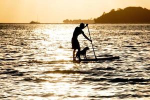 Mann paddelt mit Hund bei Sonnenuntergang in Bora Bora Französisch-Polynesien foto