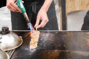 hände des kochs, der brennerkocht und kobe-rindfleisch auf einer heißen pfanne zum verkauf für kunden auf dem kuromon-markt verbrennt. kobe beef stick bar-bq ist beliebt bei touristen, die nach japan kommen. foto