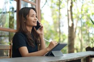 asiatische Frauen sitzen und arbeiten gerne in einem Café. Es gibt grüne Bäume, umgeben von Natur. Unternehmensplanung ist eine gute Idee. foto