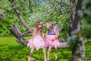 Kleine entzückende Mädchen, die auf blühendem Baum im Apfelgarten sitzen foto