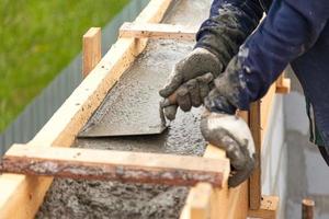 Arbeiter nivelliert Beton in Schalung mit einer Kelle foto