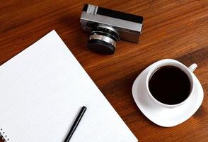 retro film fotokamera, tasse kaffee und notizbuch mit bleistift auf braunem tisch. Ansicht von oben. foto