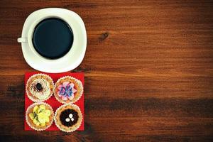 Tasse Tee oder Kaffee und vier Cupcakes auf braunem Tisch. Ansicht von oben foto