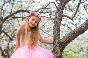Kleines entzückendes Mädchen, das auf blühendem Baum im Apfelgarten sitzt foto